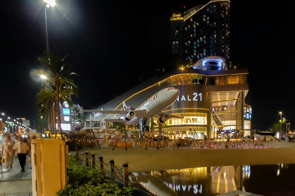 Illuminated Terminal 21 shopping mall in Pattaya, Thailand, with airplane replica, captured at night.